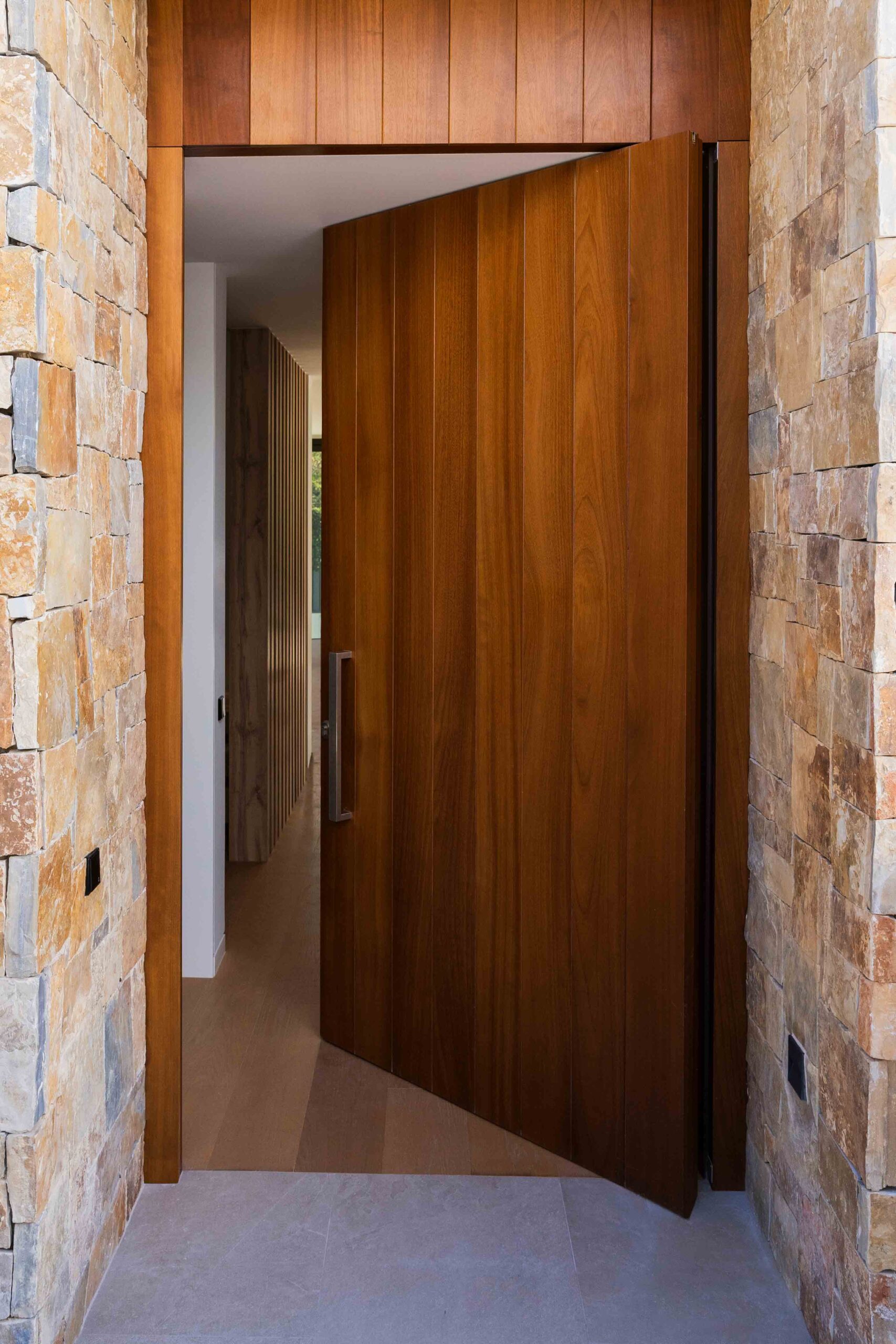 Drehtür in einem Luxushaus mit Materialien wie technischem Holz und Naturstein an der Fassade