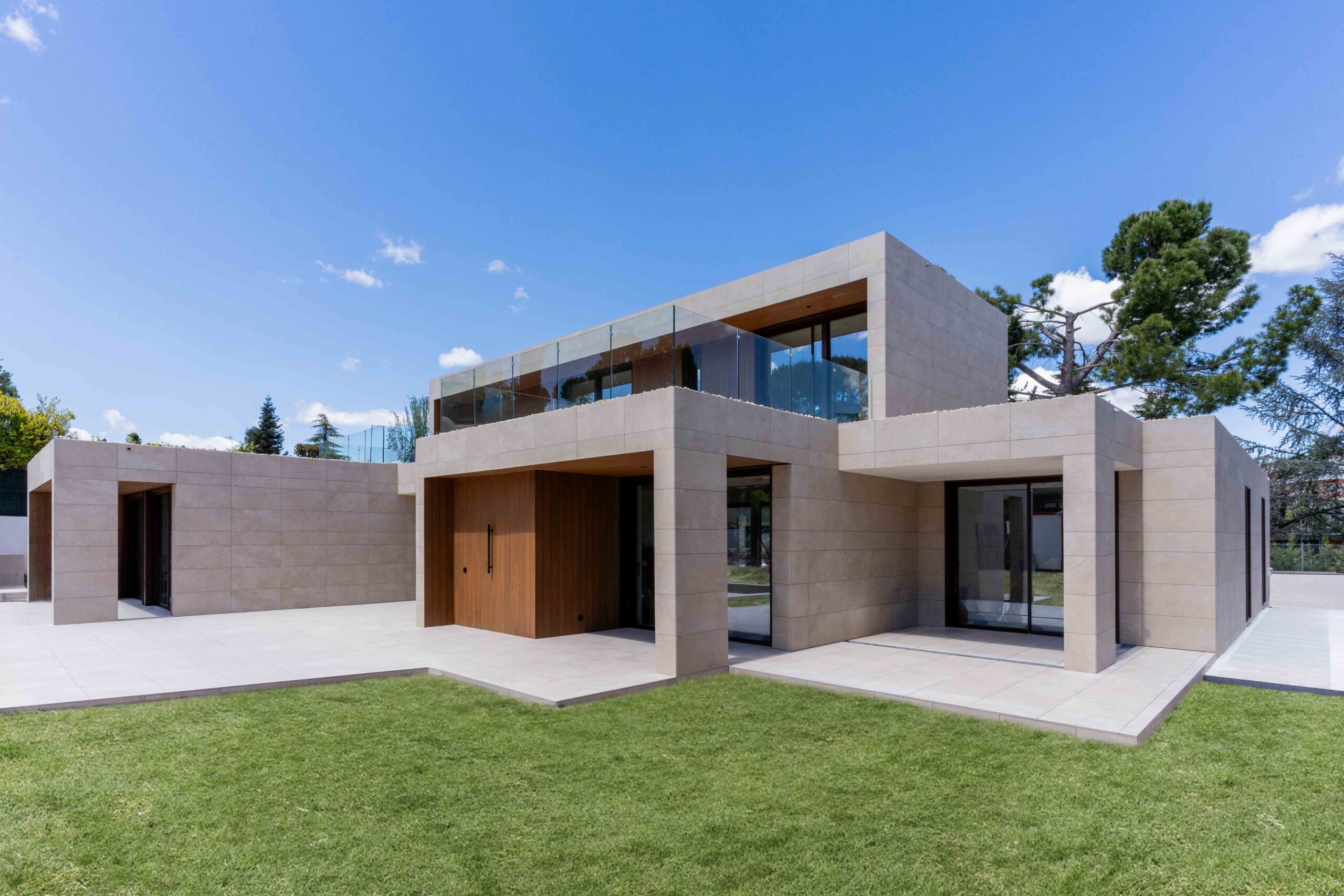 Fassade mit würfelförmigen Volumen, Seitenansicht mit Porzellanmaterialien, Kunstrasen und technischem Holz im Außenbereich.