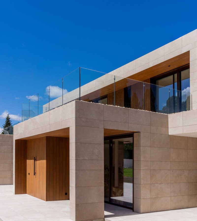 Fassade mit würfelförmigen Volumen, Seitenansicht mit Porzellanmaterialien, Kunstrasen und technischem Holz im Außenbereich.